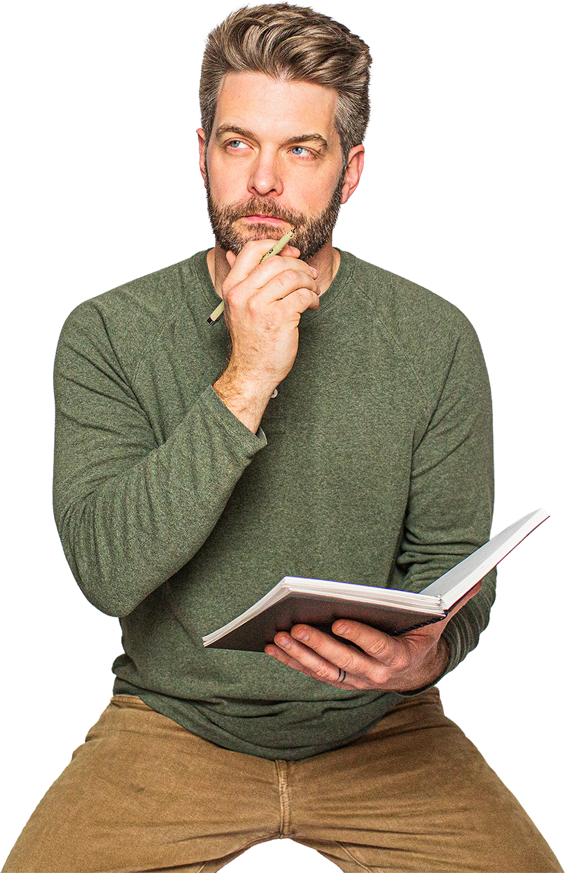Kyle Scheele artist and creative holding his chin with one hand thoughtfully with a pen in it and an open journal in his other hand.